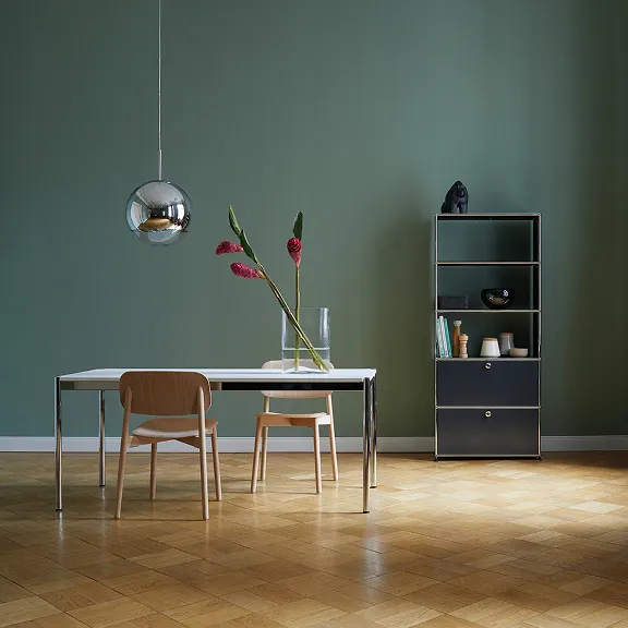 USM Haller Tisch, über dem eine Discokugel hängt. Im Hintergrund steht ein schwarzes USM Haller Regal.